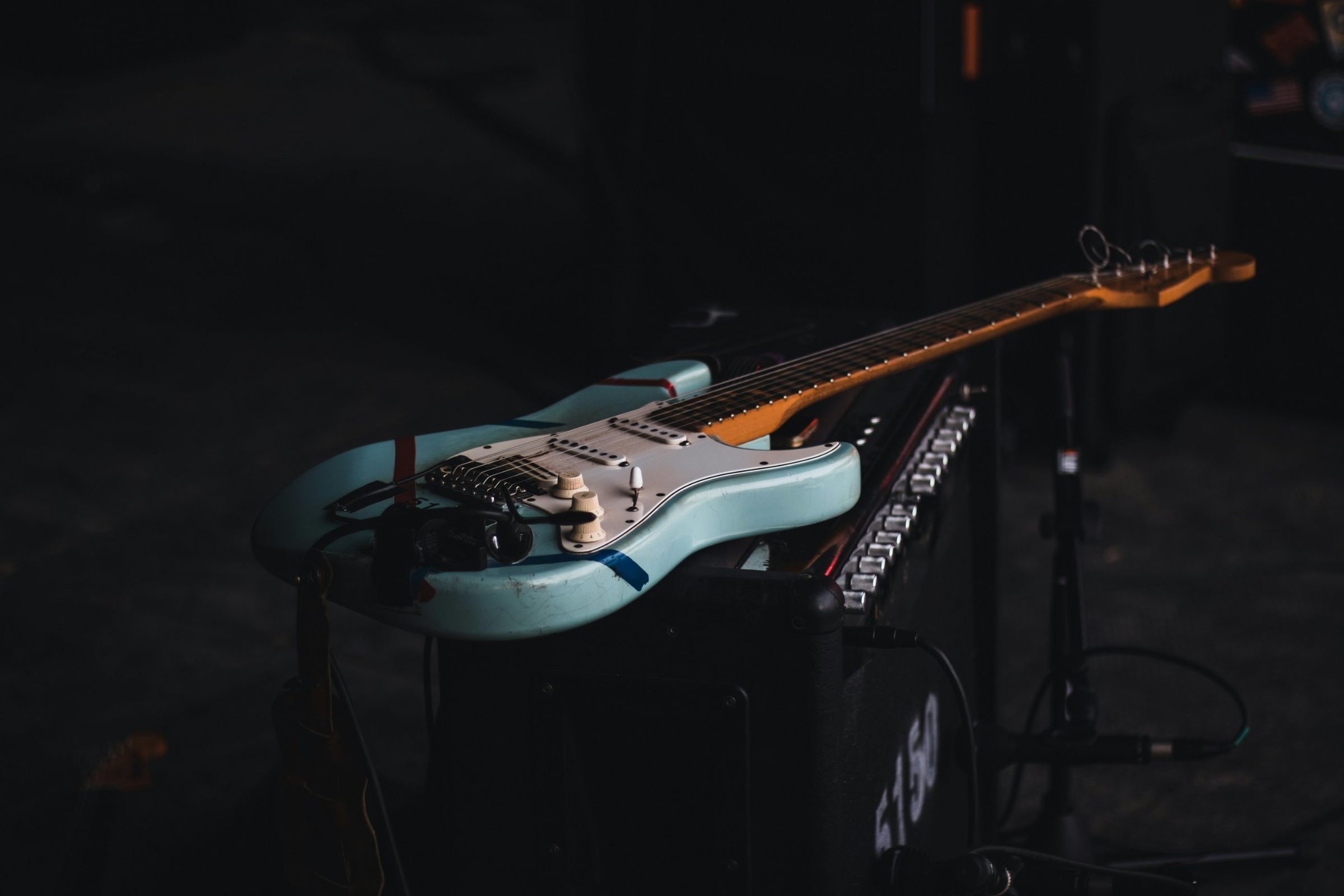 An electric guitar resting on an amp in a dark room