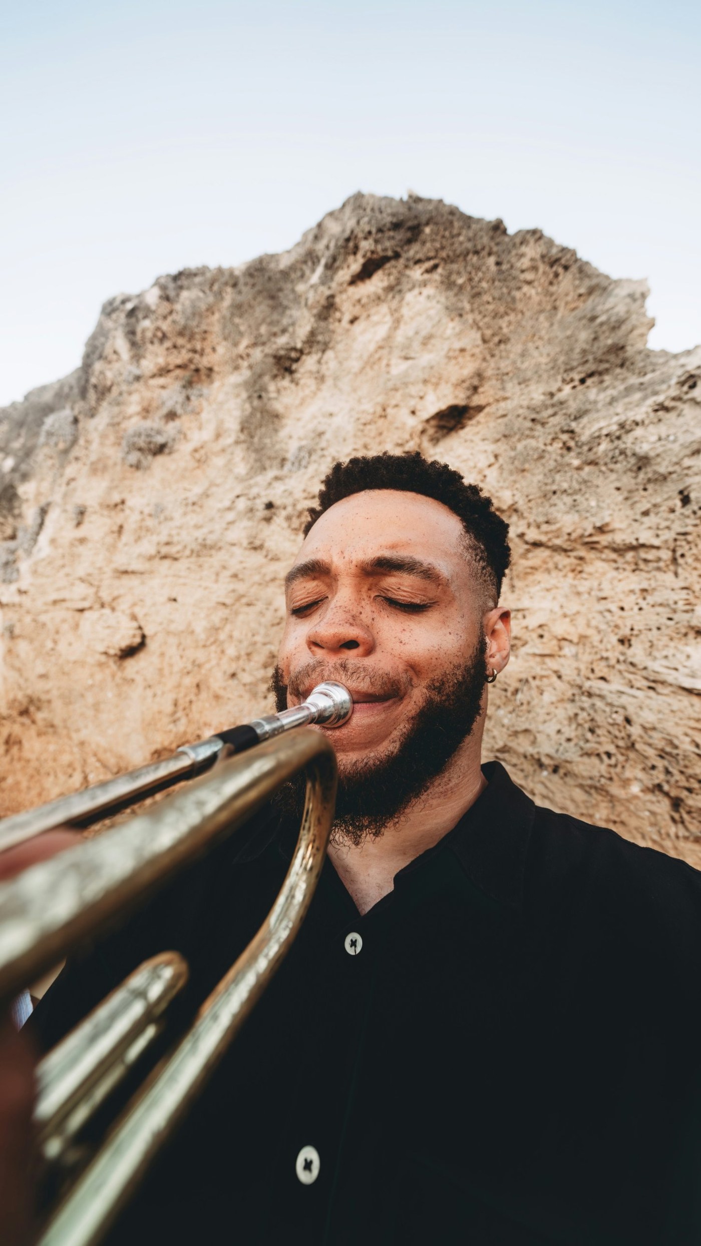 A trumpet player, eyes closed, against a rock face